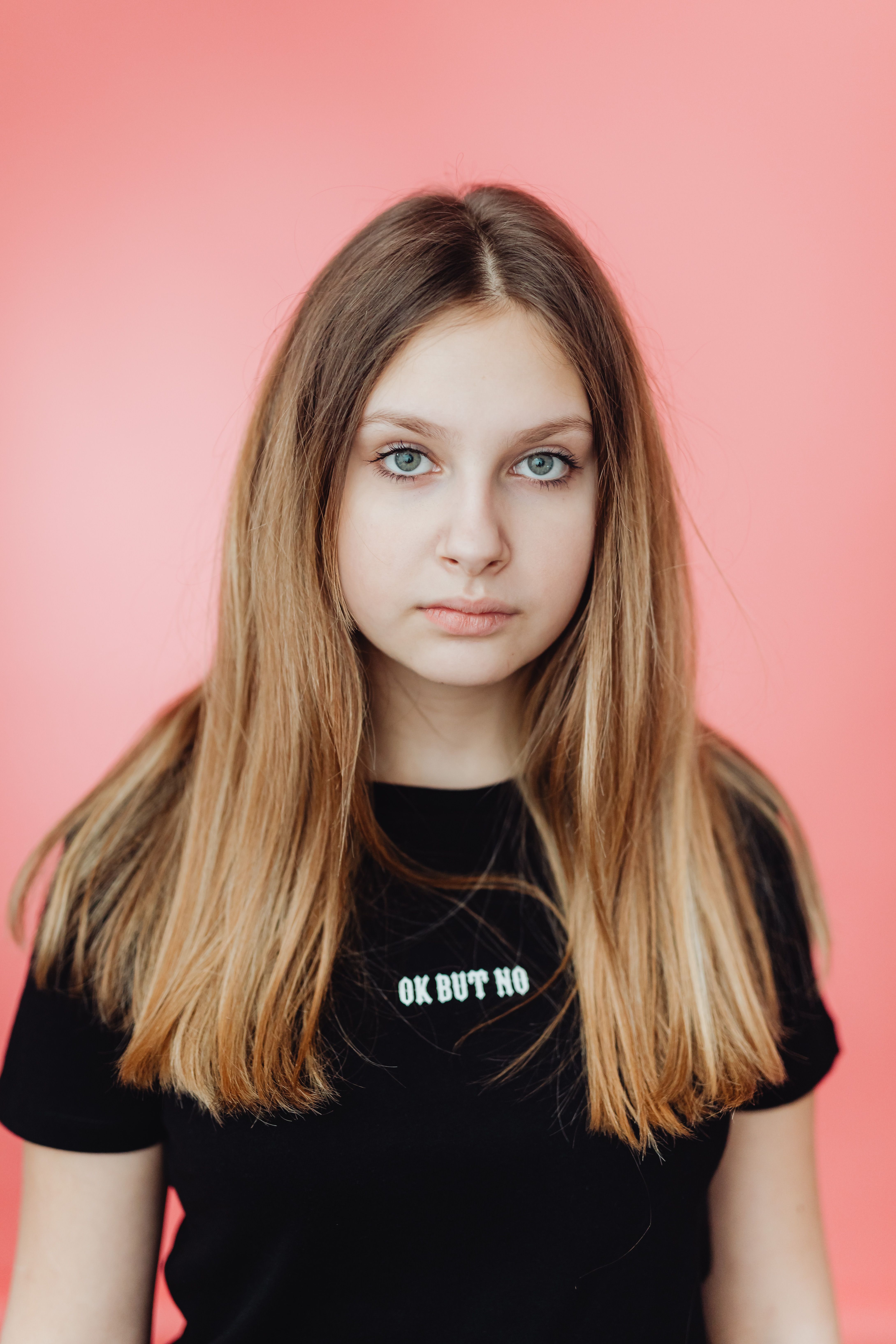 A young woman posing against a pink background in a studio setting.
