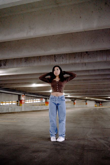 Stylish woman in a crop top and jeans poses confidently in a parking garage.