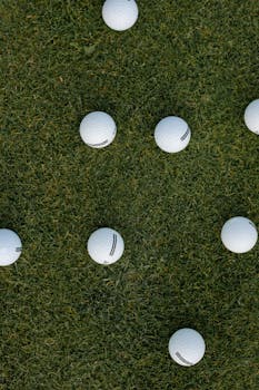 Scattered golf balls on lush green grass viewed from above, offering an ideal sports background.