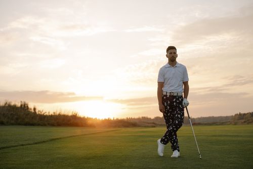 Free A golfer stands on a golf course holding a club during a dramatic sunset scene. Stock Photo