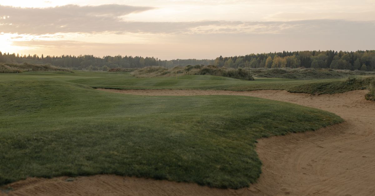 A tranquil golf course landscape at sunset, showcasing green fairways and gentle sandtraps.