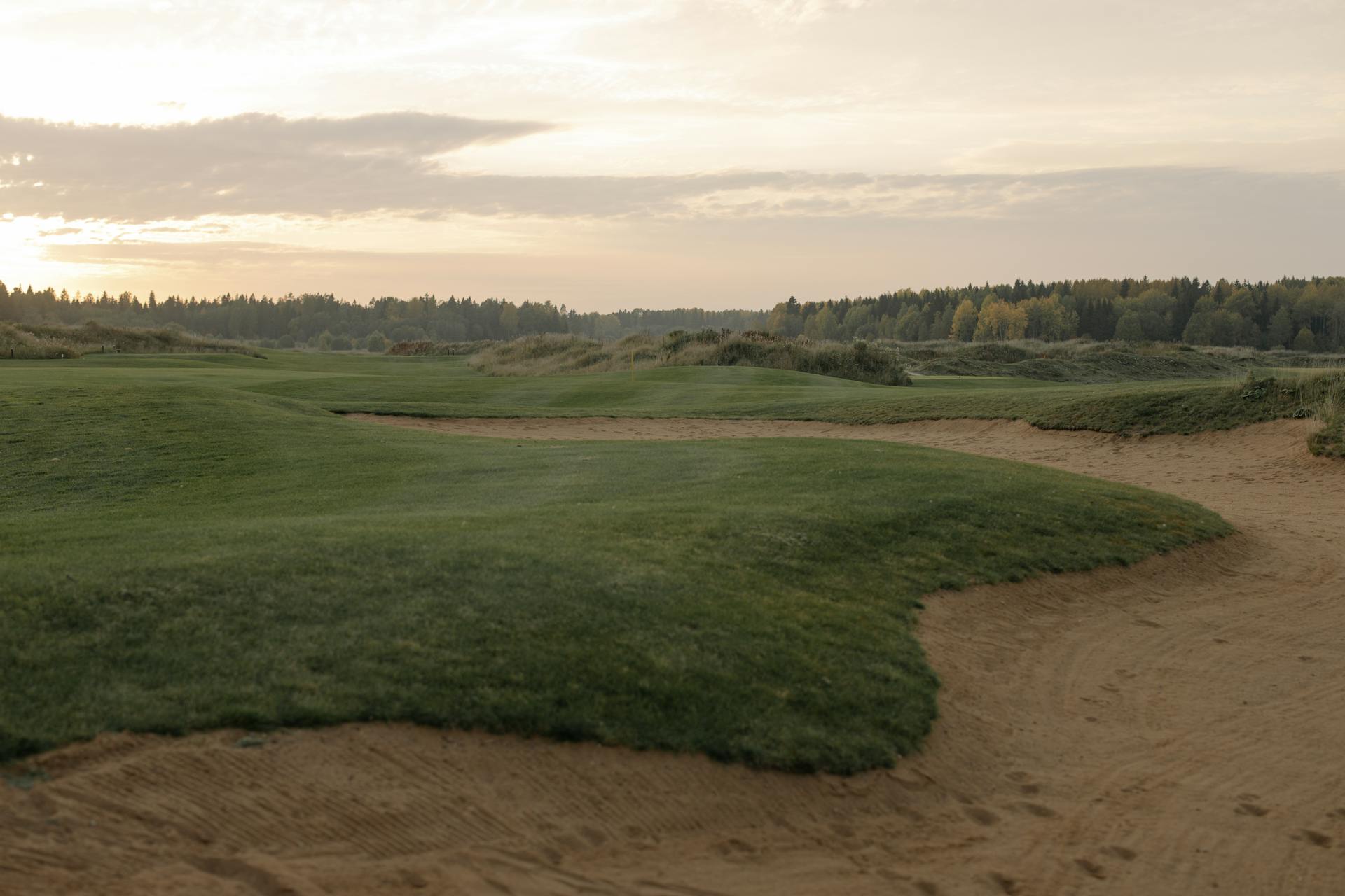 A tranquil golf course landscape at sunset, showcasing green fairways and gentle sandtraps.