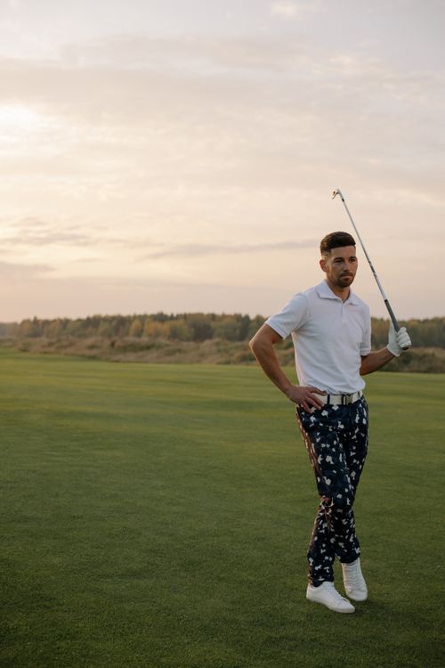 Free A fashionable male golfer poses with a golf club on a course at sunset, exuding confidence and style. Stock Photo