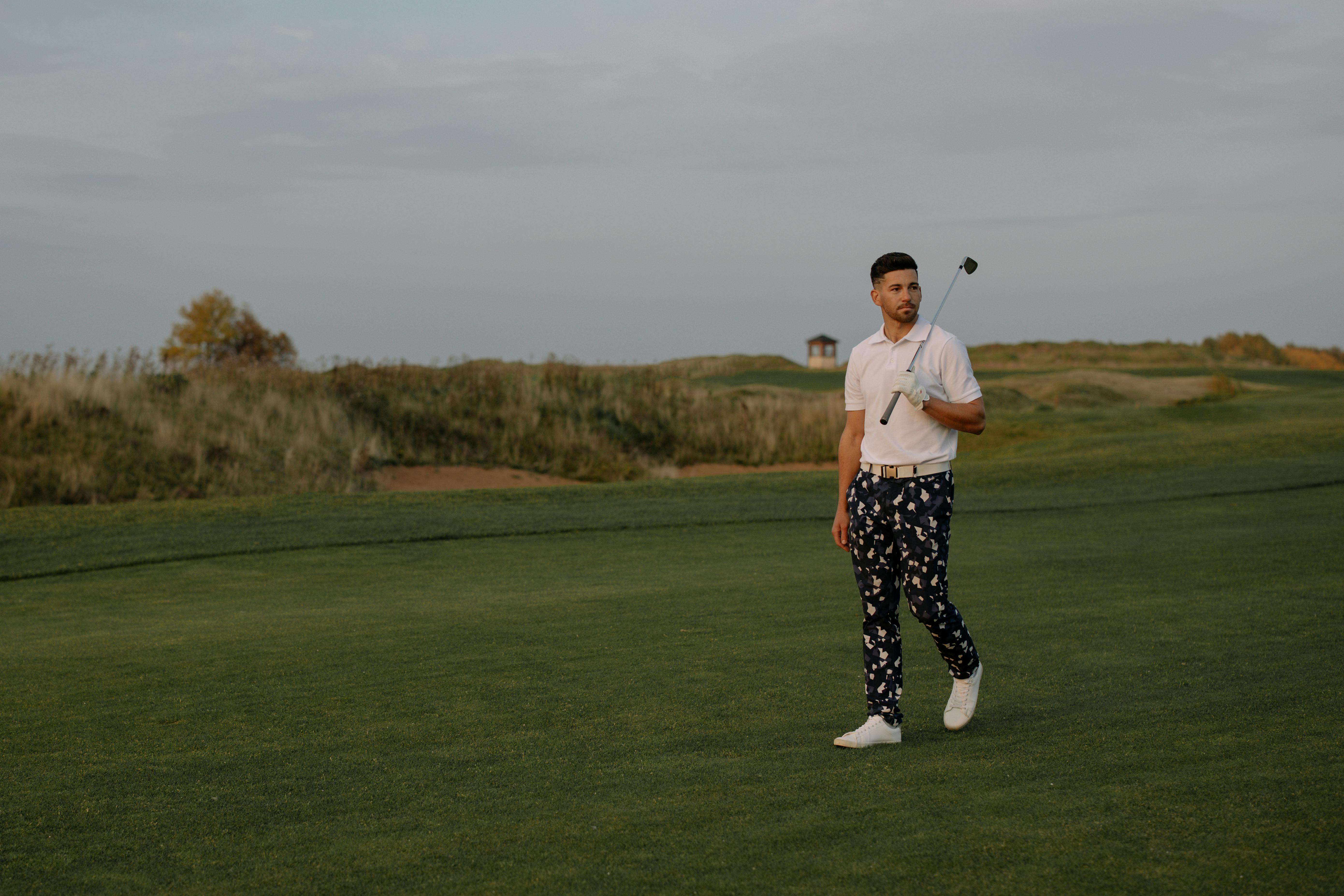 A golfer walking across a golf course during sunset, holding a golf club. Ideal for sports and lifestyle content.