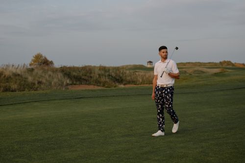 Free A golfer walking across a golf course during sunset, holding a golf club. Ideal for sports and lifestyle content. Stock Photo