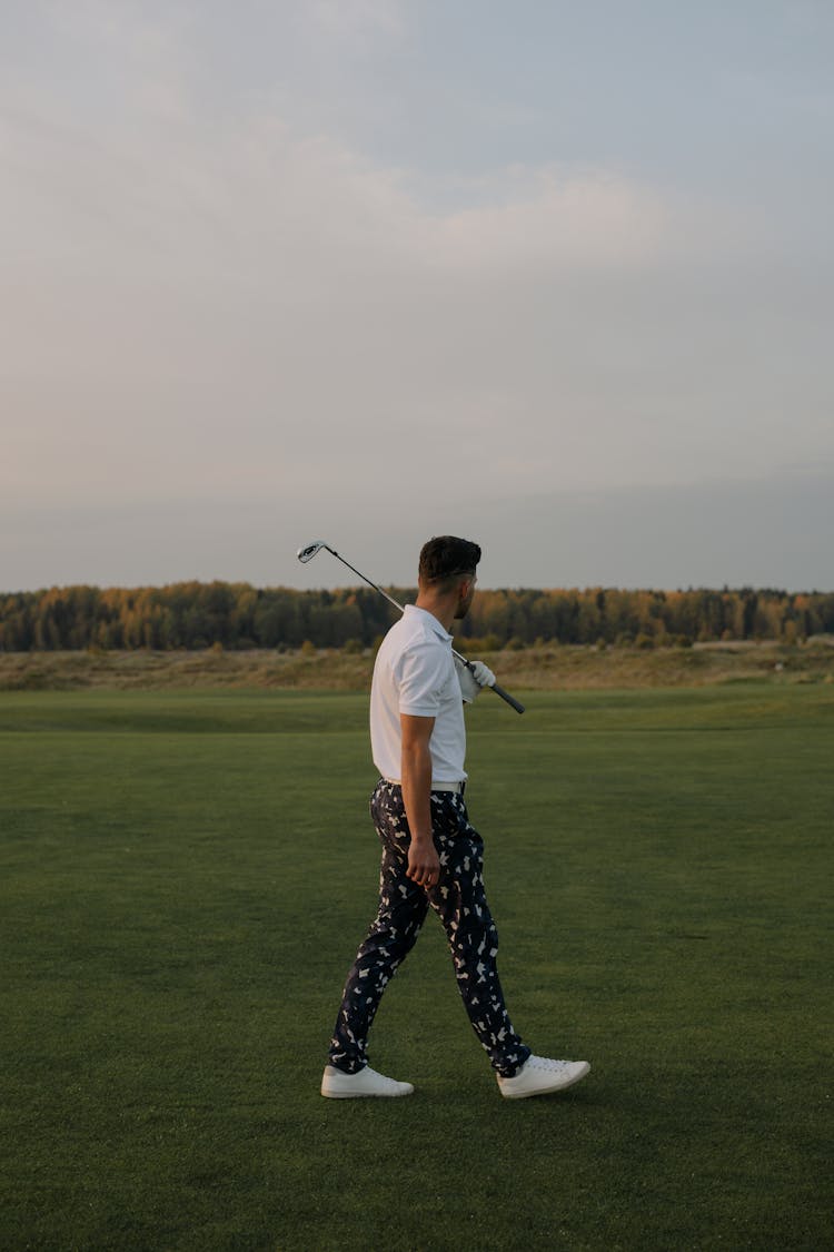 Golfer Holding A Golf Club Walking On A Grass Field 