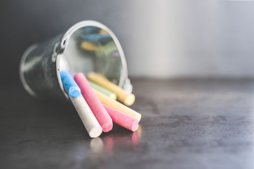 Free Vibrant chalk sticks in various colors spilling from a metal bucket on a dark surface. Stock Photo