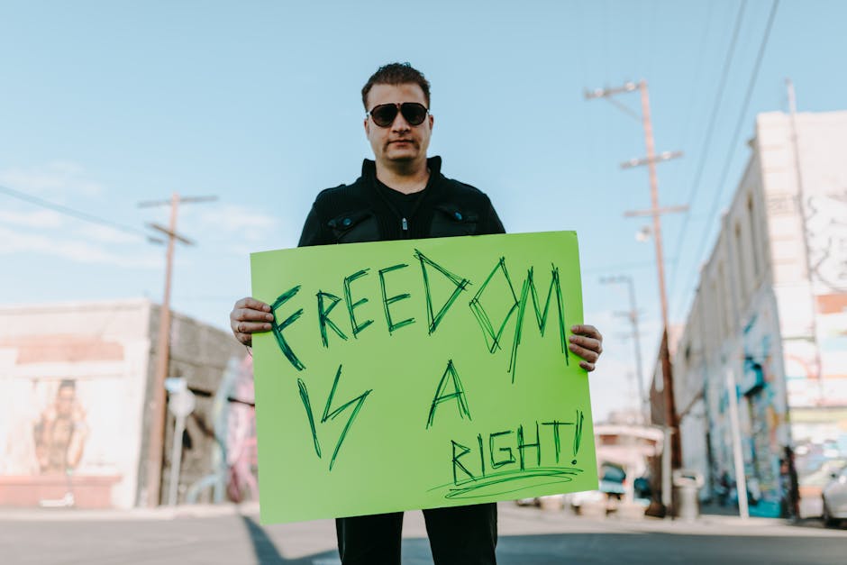 A man holds a bright protest sign stating 'Freedom is a Right!' outdoors.