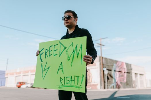 Man standing outdoors holding a sign reading 'Freedom is a Right' in a protest.