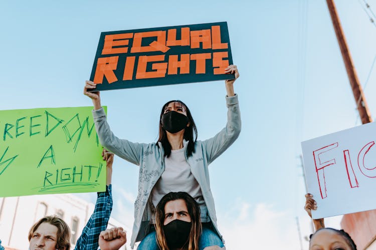 A Person Carrying A Protester Holding A Placard On His Shoulders