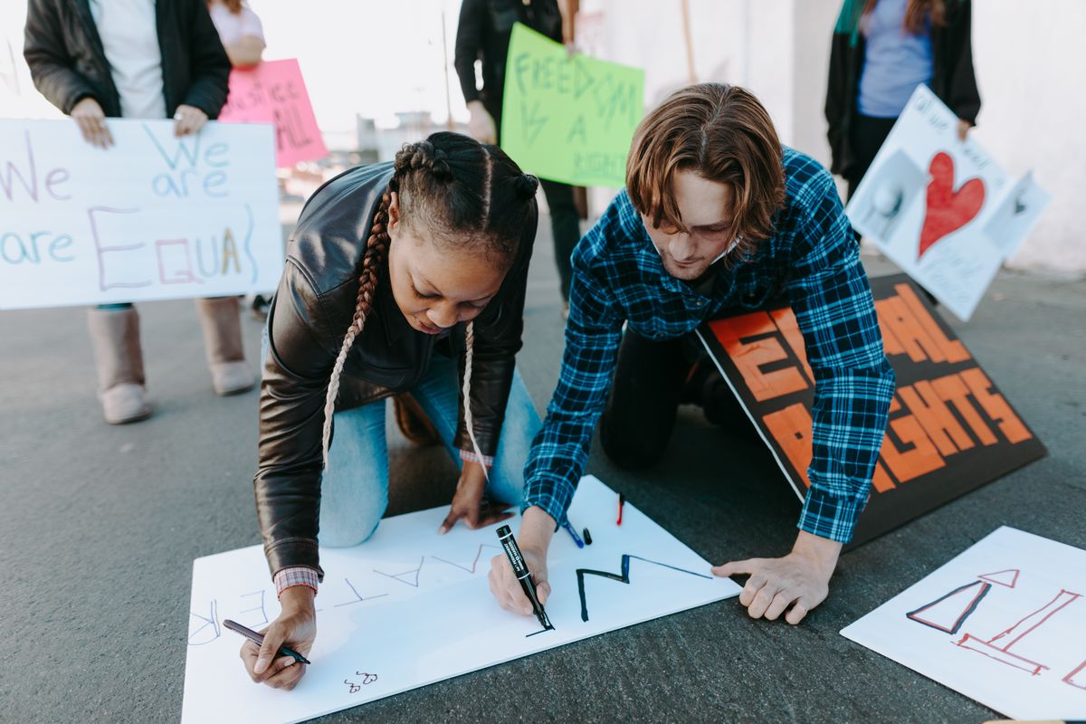 handwritten protest signs taped to chainlink fence