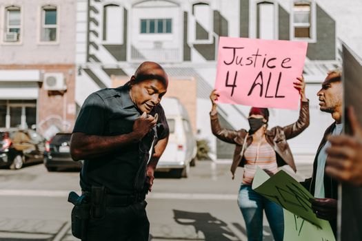 Protestors with signs engage with a police officer on an urban street.
