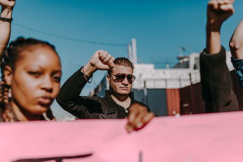 Free A group of diverse protesters holding a banner, raising fists in outdoor demonstration. Stock Photo