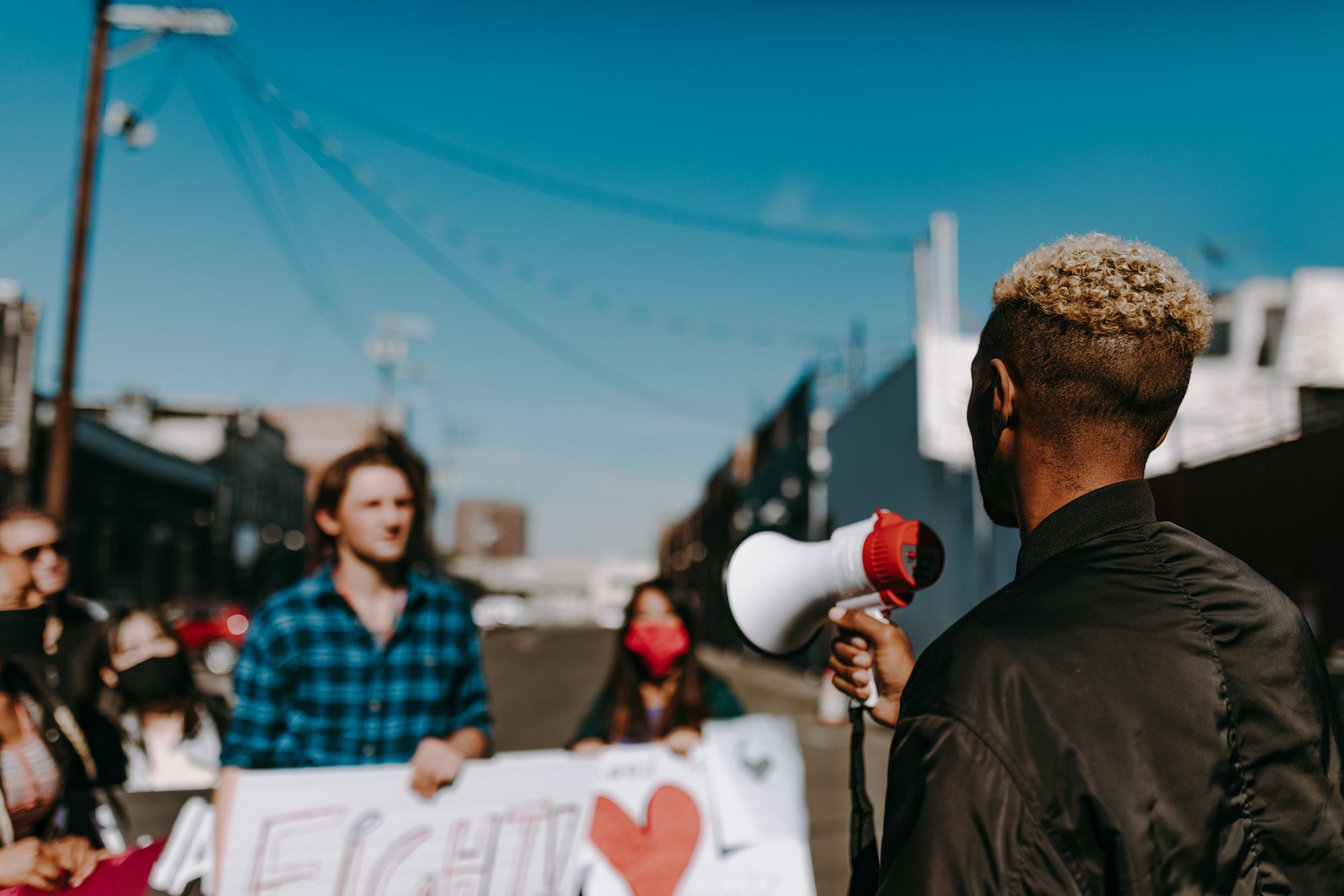 A diverse group of people protesting in an urban setting, with a focus on a speaker using a megaphone.