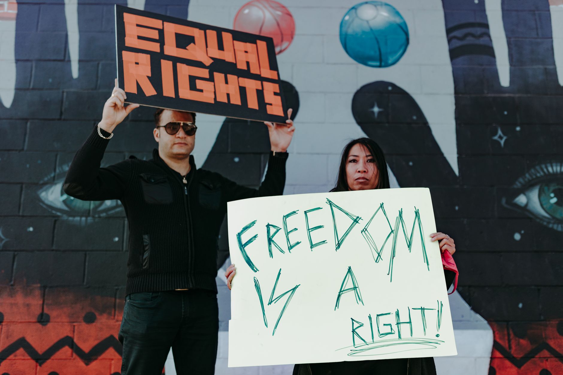 شخصان يرفعان لافتتين «Equal Rights» و«Freedom is a right» أمام جدارية