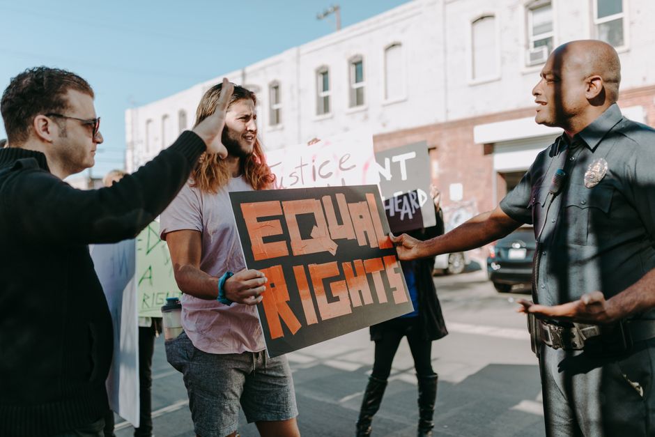 People at a protest holding 'Equal Rights' sign and discussing with a police officer outdoors.