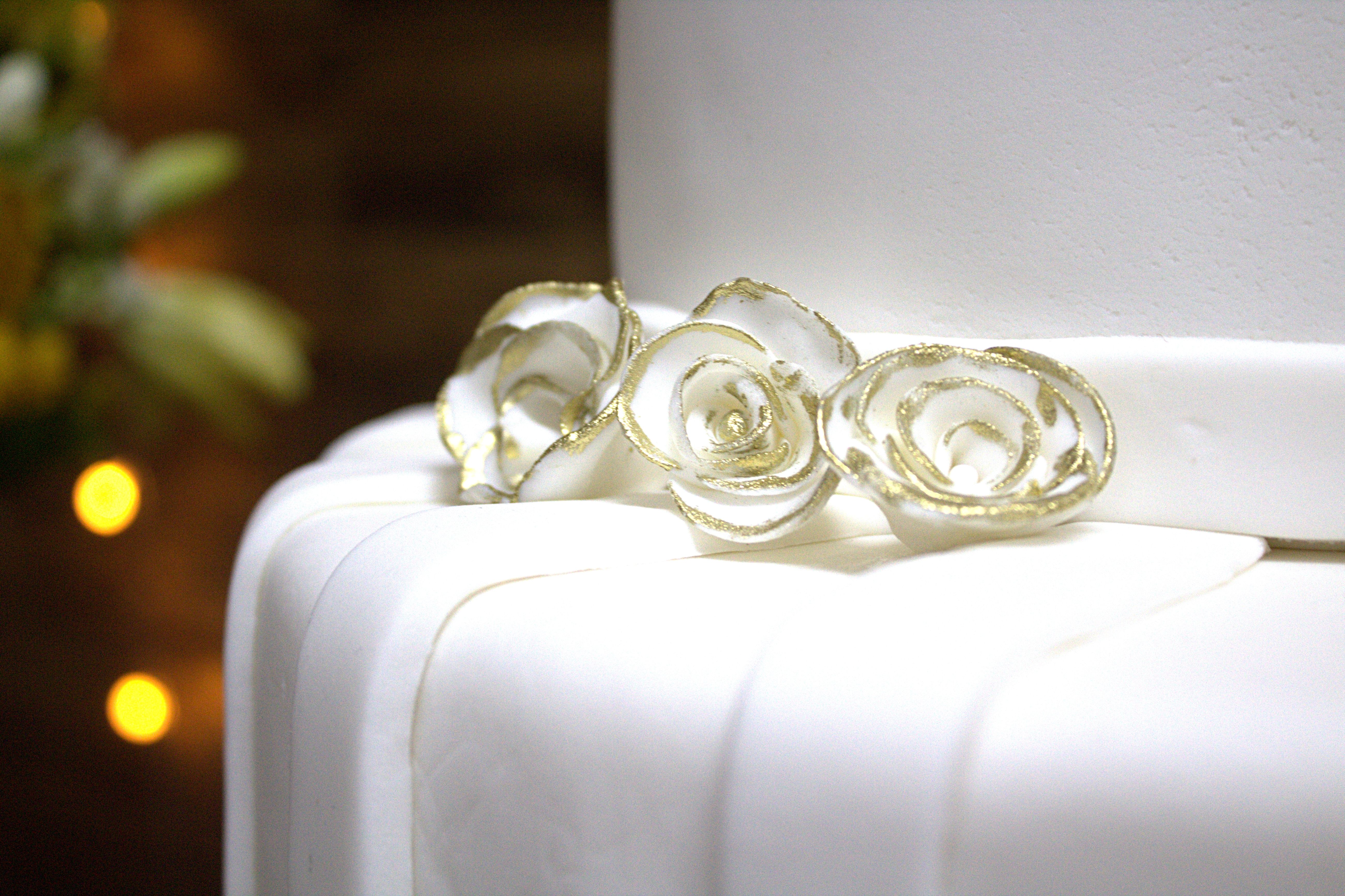Close-up of a beautifully decorated wedding cake adorned with gold-trimmed white fondant flowers.