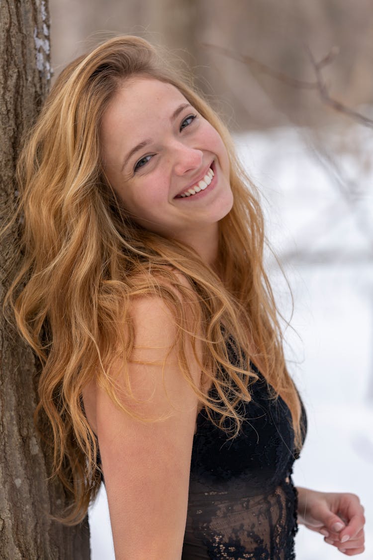 Stylish Woman In Black Top Standing Near Tree In Winter Forest