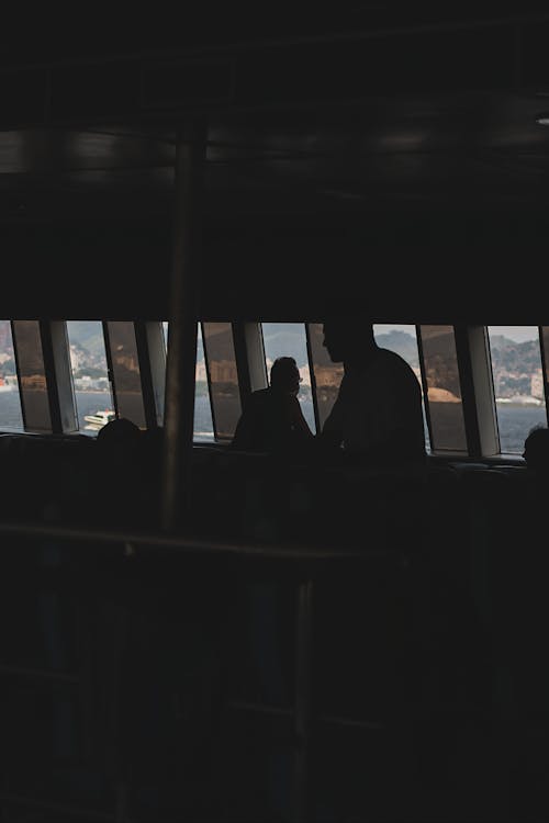 Silhouettes of unrecognizable passengers inside power boat travelling on river in sunny day