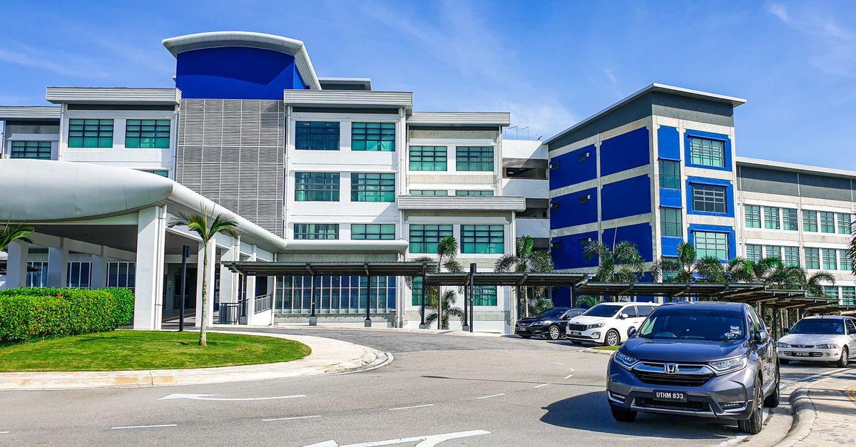 Modern building with blue accents and parked cars in Johor, Malaysia, under a clear sky.