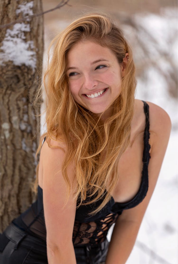 Cheerful Woman In Black Top Near Tree In Winter Woodland