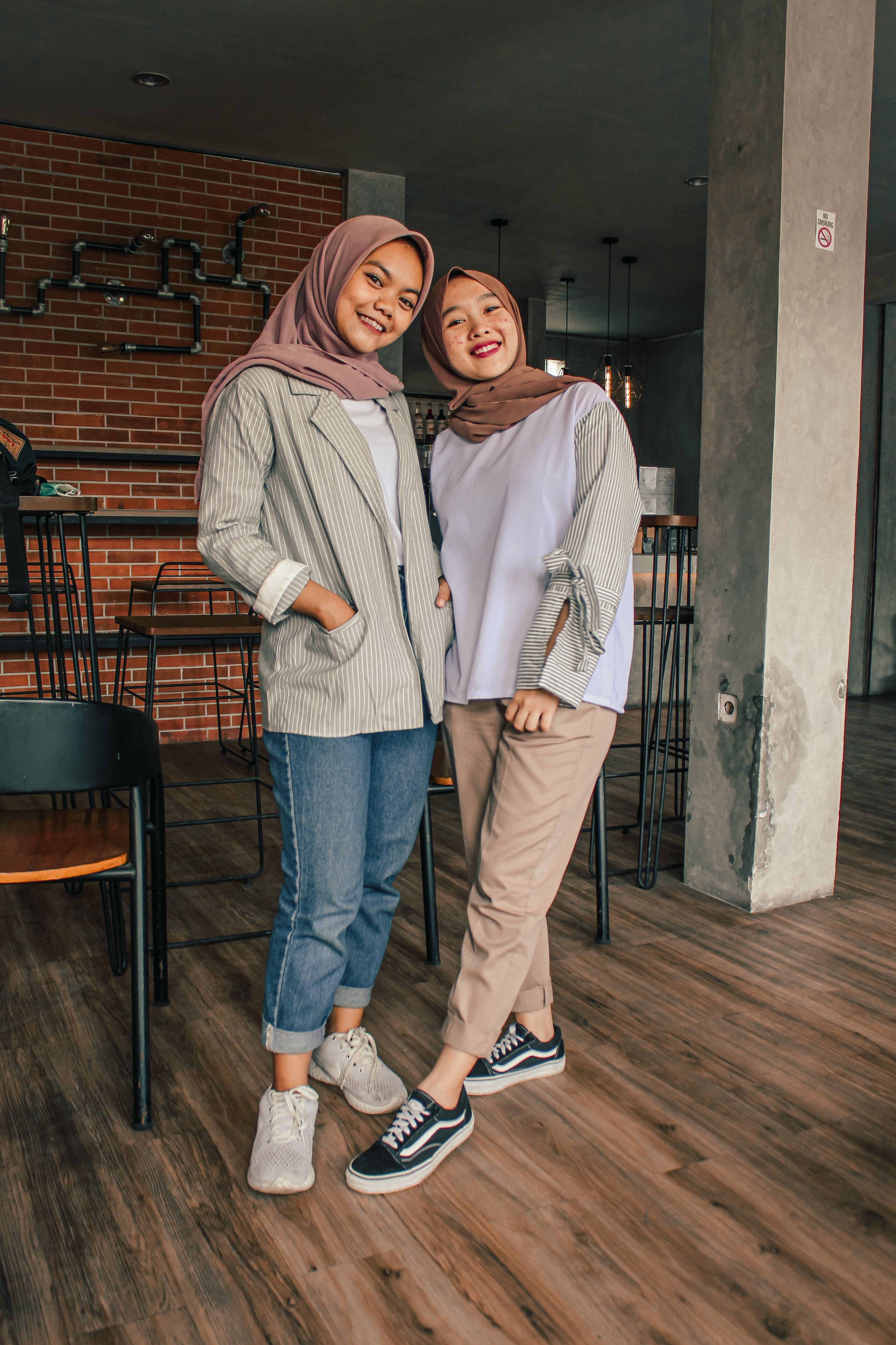 Two teenage girls in hijabs smiling and posing indoors with a modern setting.