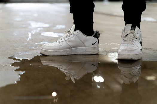 A pair of white sneakers reflected in a puddle on an indoor surface, creating an artistic perspective.