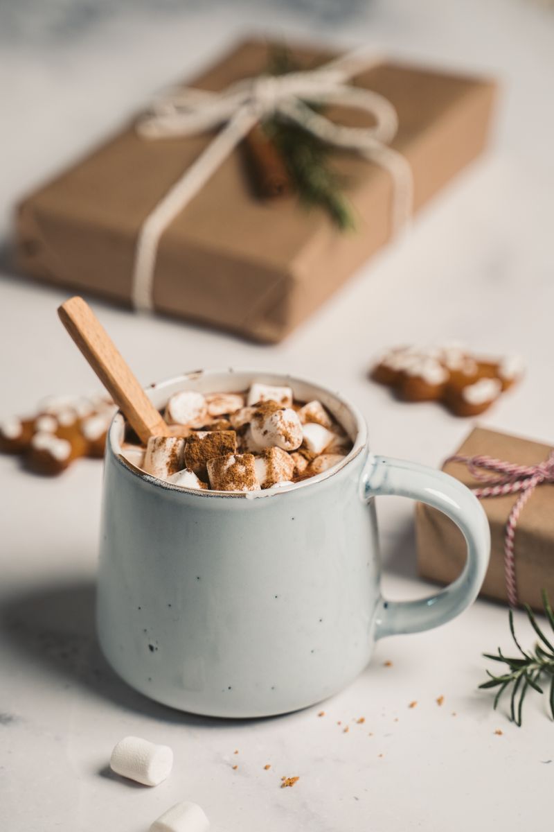Hot chocolate topped with marshmallows beside Christmas gifts