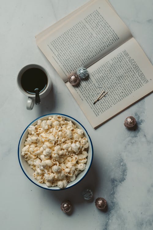 Bowl of Popcorn Beside Coffee Cup and Book