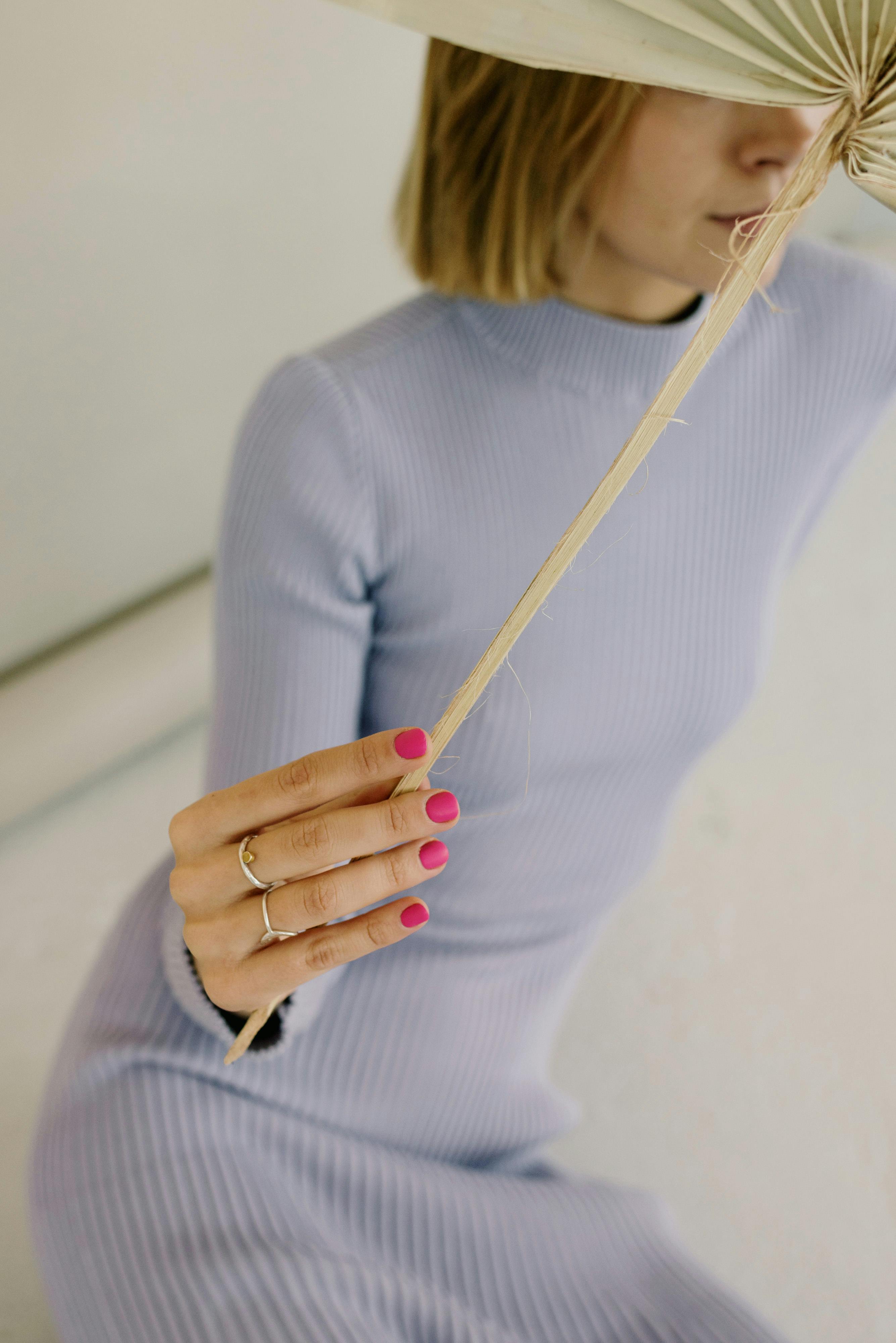A stylish woman in a lilac dress with pink nails holding a leaf, showcasing modern elegance.