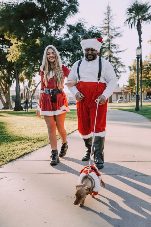 Free Couple dressed in Santa attire strolling with their dog on a sunny day. Stock Photo