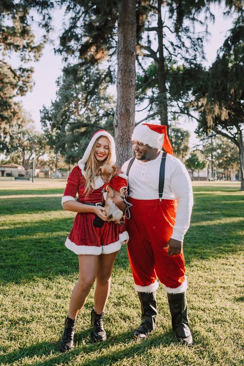 Free A joyful Santa and elf in a park holding a small dog celebrating Christmas outdoors. Stock Photo