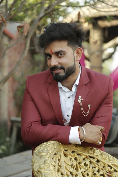 Free Portrait of a man smiling in a red suit outdoors, leaning on a decorative chair. Stock Photo