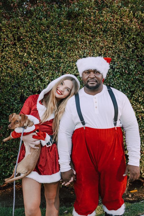 Free A cheerful couple in Christmas costumes holding a dachshund dog outdoors. Stock Photo