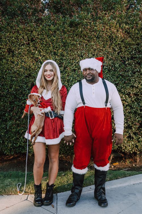 Free A cheerful couple in Santa outfits holding a dog outdoors during the day. Stock Photo
