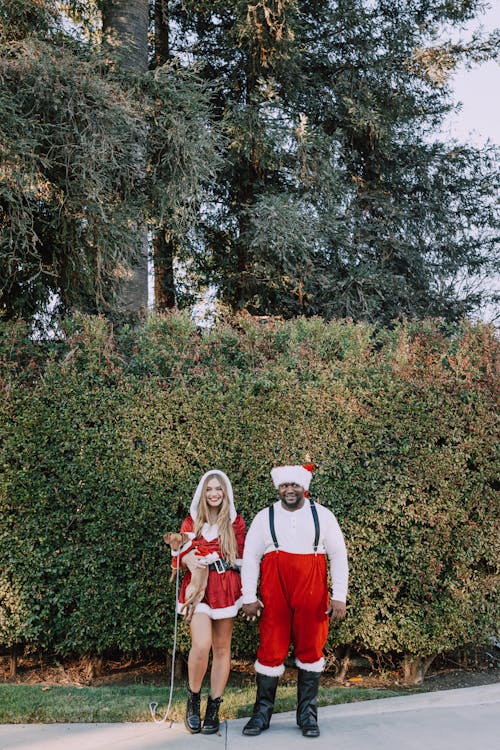 A Couple in Santa Costumes Standing Near a Hedge