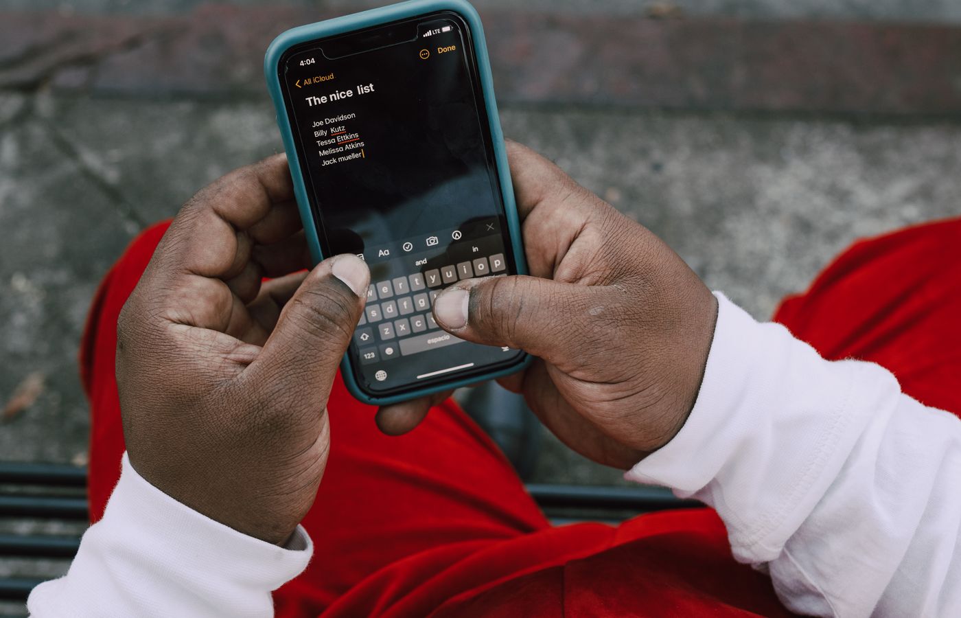 A person typing on a smartphone outdoors, wearing a red and white outfit, capturing a close-up view.