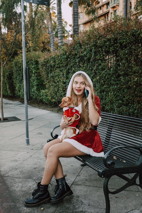 Woman in Red Dress Sitting on Black Metal Bench Holding Brown Dog