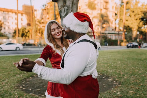 A Couple Holding Hands while Wearing Santa Costumes