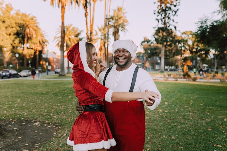 A Couple Wearing Santa Costume Dancing On A Park