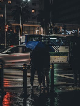 People standing in the rain with umbrellas on a Jakarta street at night. Urban life captured with motion blur.