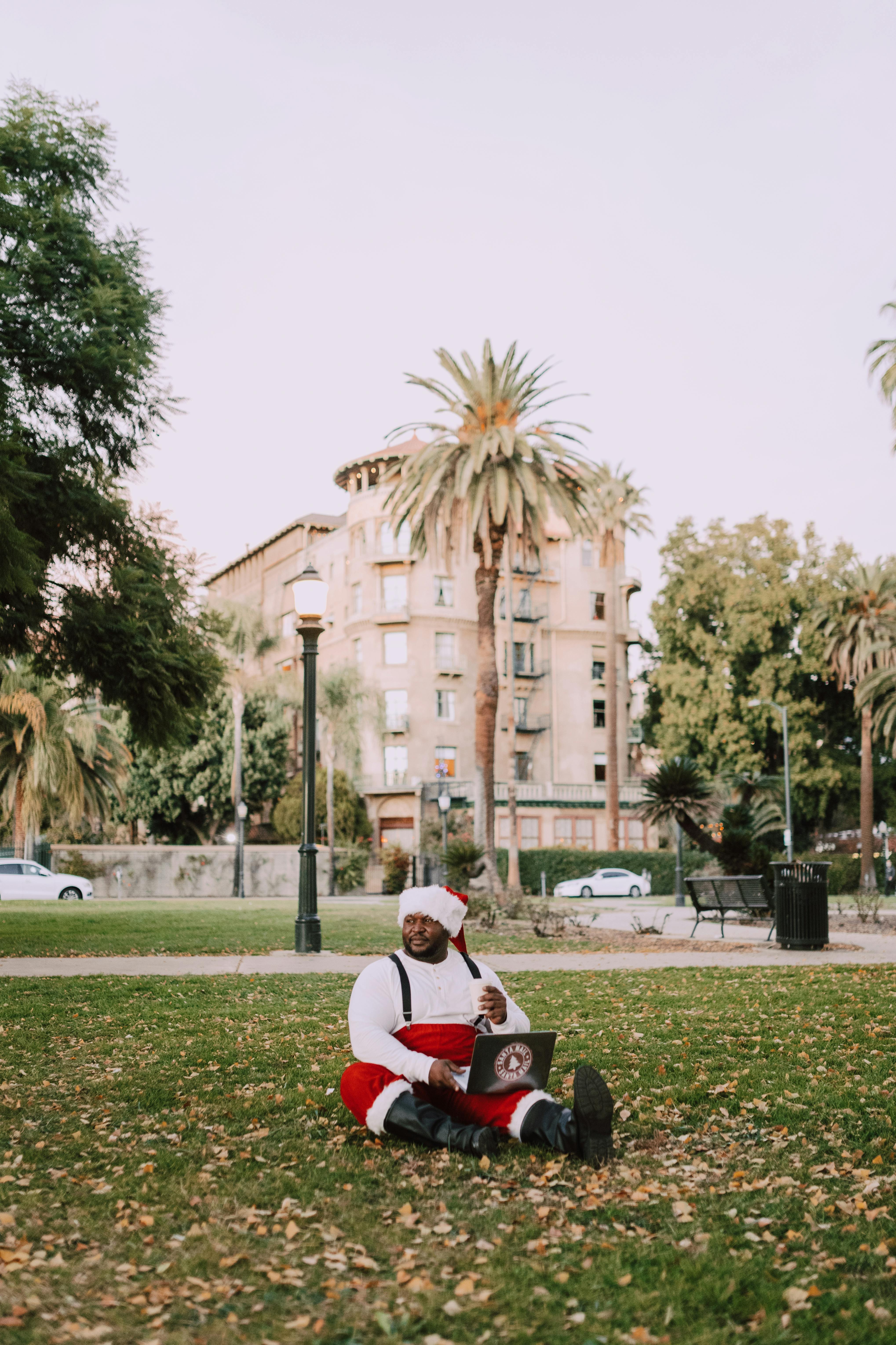 Santa Claus in an urban park enjoying leisure time with a laptop.