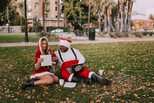 A Man and a Woman Dressed as Santa Sitting on Grass
