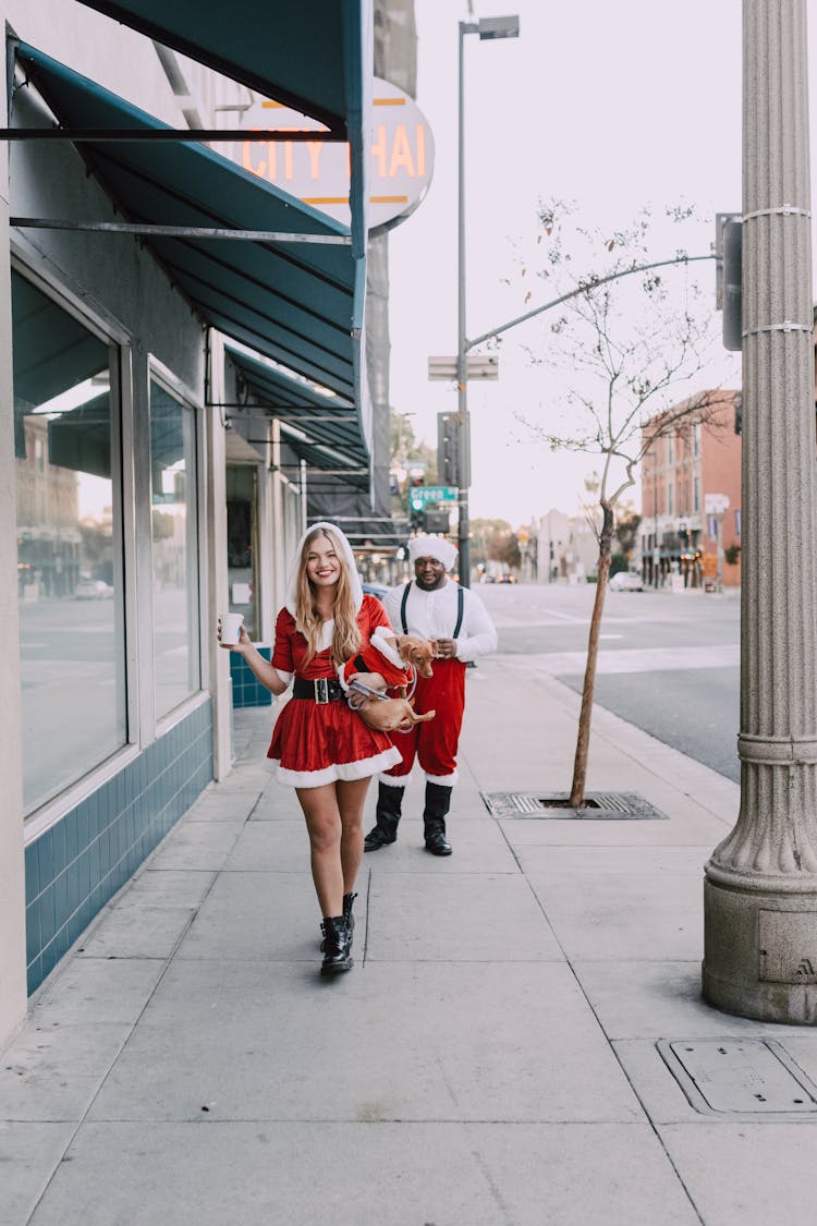 A Man And A Woman In Santa Costume Walking On Sidewalk