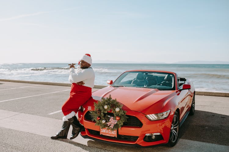 Man In Santa Costume Leaning On A Car