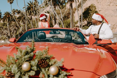 A Man and a Woman Wearing Santa Hats in a Red Convertible

