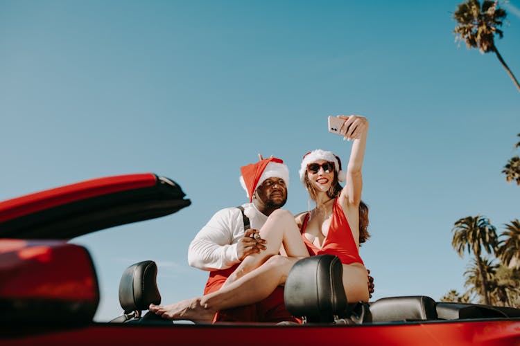 Man And Woman Taking Selfie Beside Red Car