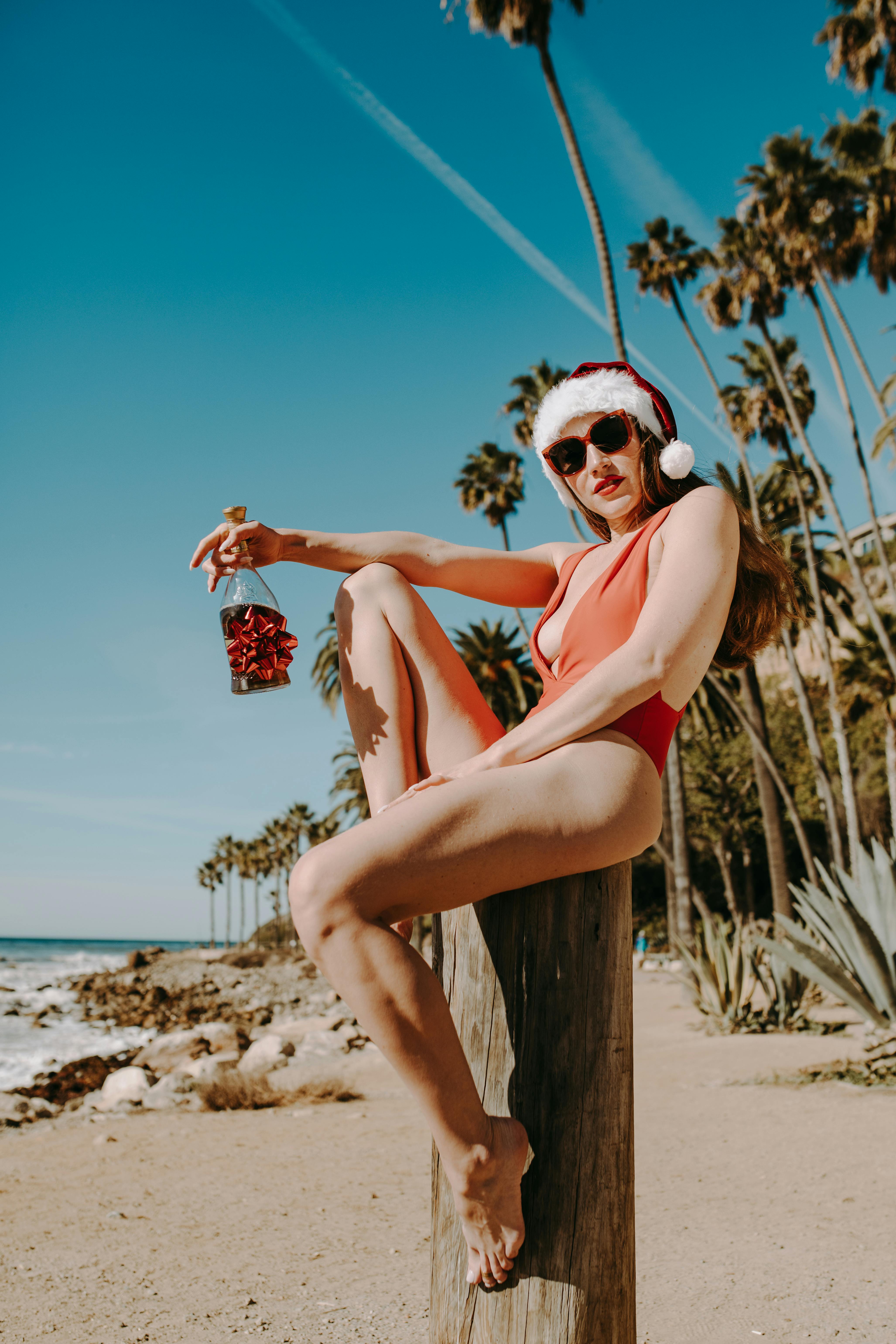 woman in orange bikini sitting on brown wooden log on beach