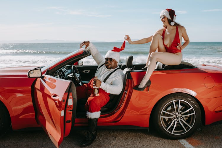 Man And Woman In Santa Outfits Sitting In A Red Convertible Car