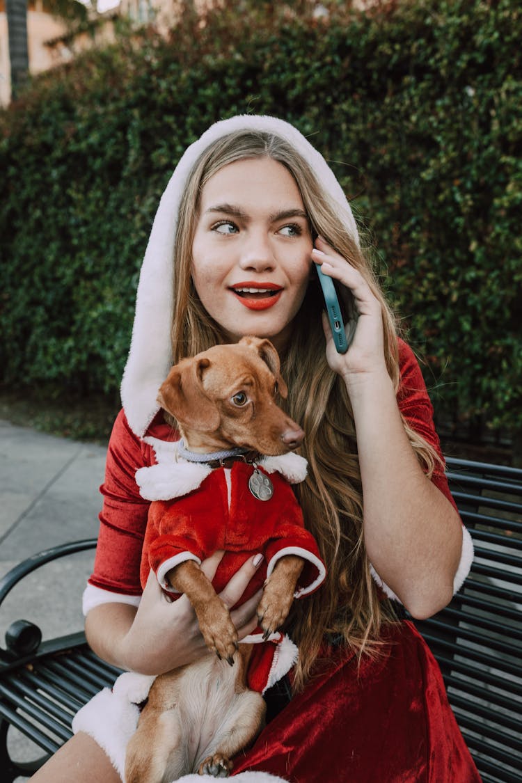 A Woman On A Phone Call Wearing Matching Santa Costumes With Her Dog